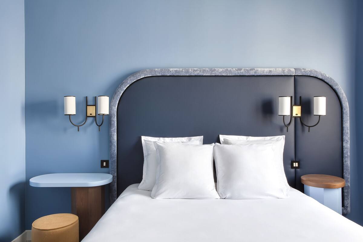 A neatly made bed with white linens, a curved headboard, and two bedside tables with lamps.