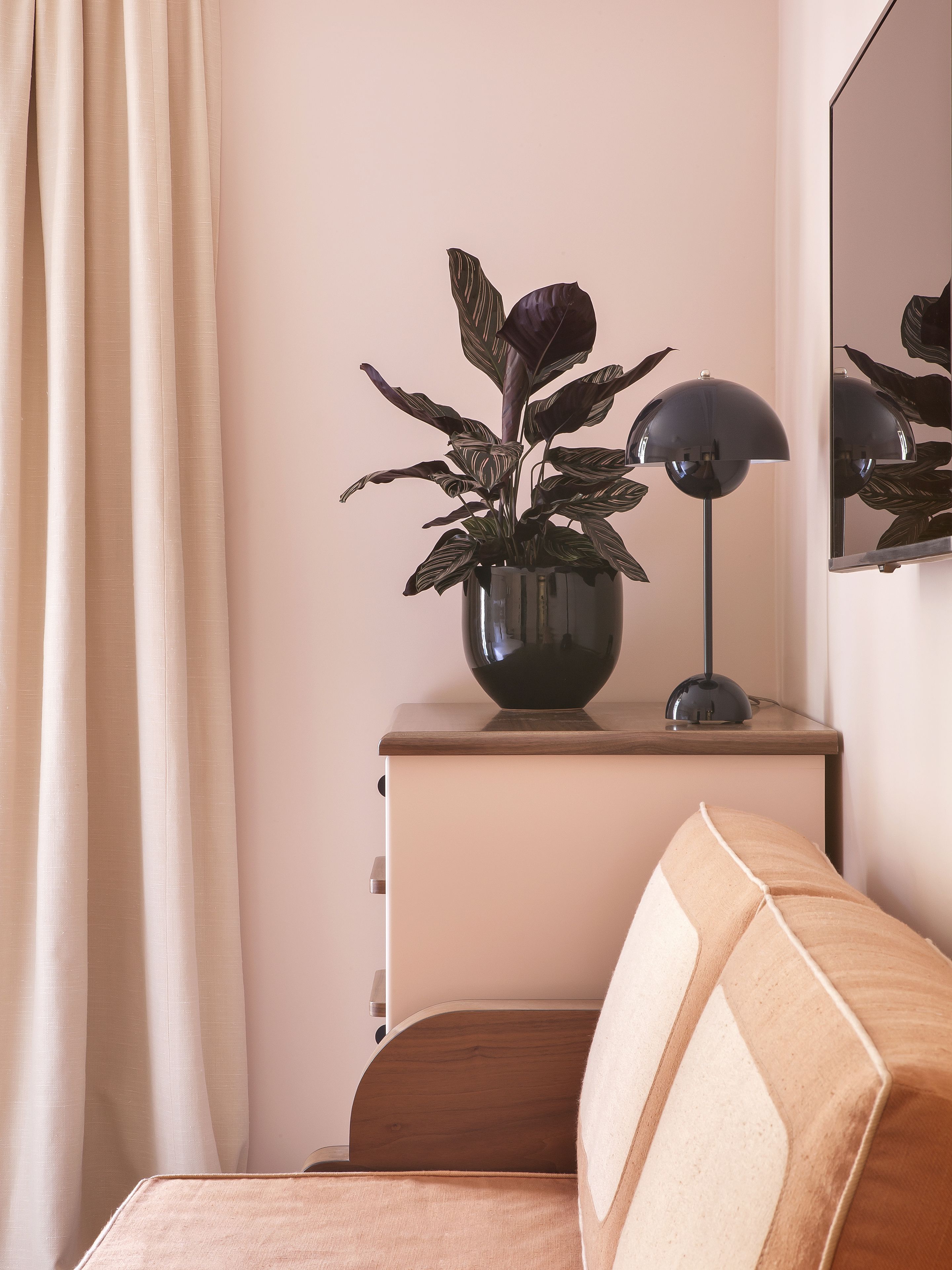 A neatly arranged bedroom with a bed, a bedside table with a lamp, a potted plant, and a mirror.