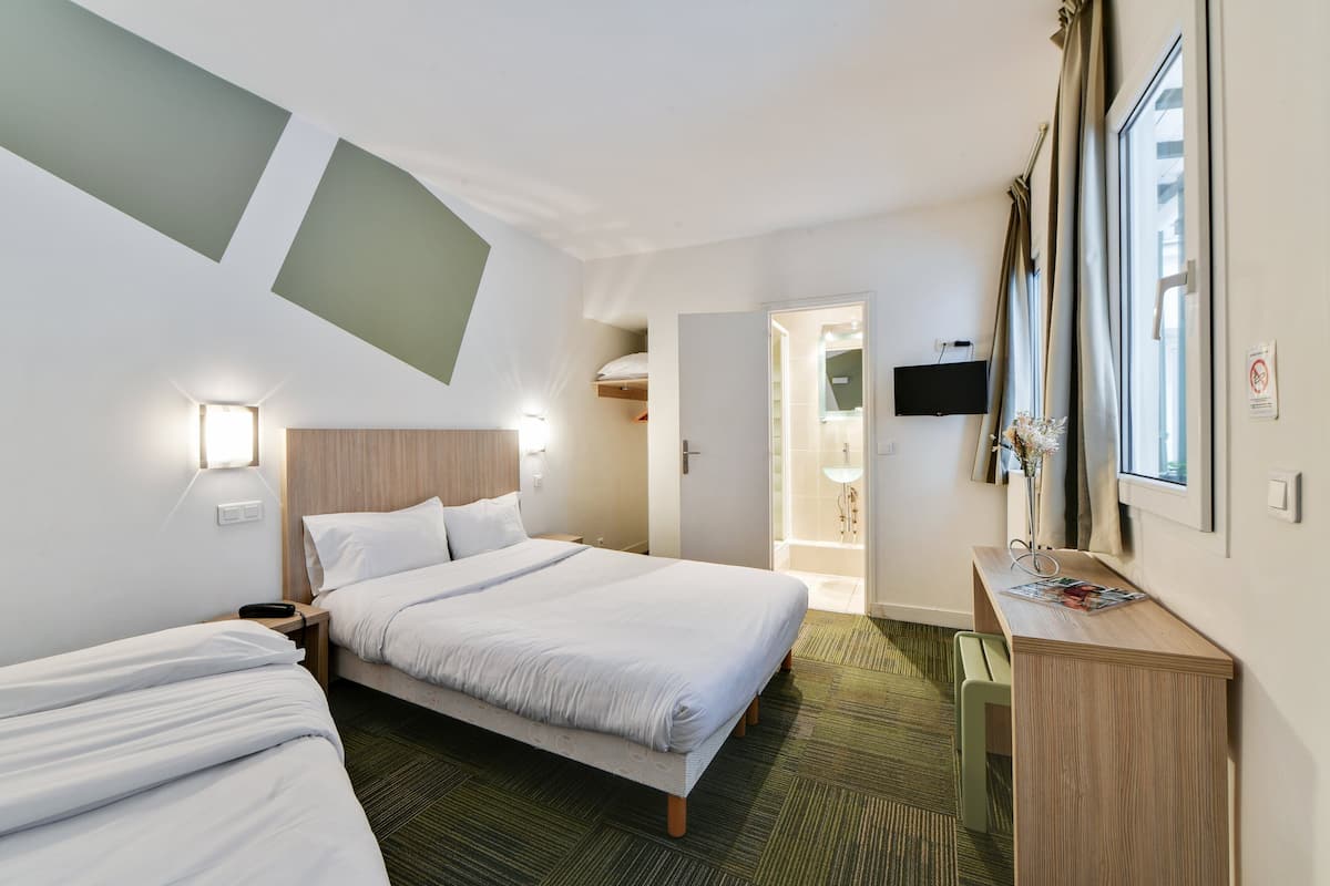A hotel room with two beds, a desk, a TV, and a bathroom visible through an open door.