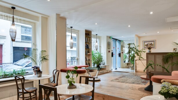 En rummelig opholdsstue med trægulv, et rundt bord med stole, en rød sofa og flere krukker med planter.