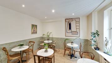 Comedor con mesas redondas y sillas de mimbre, rodeado de plantas en macetas y obras de arte en las paredes.