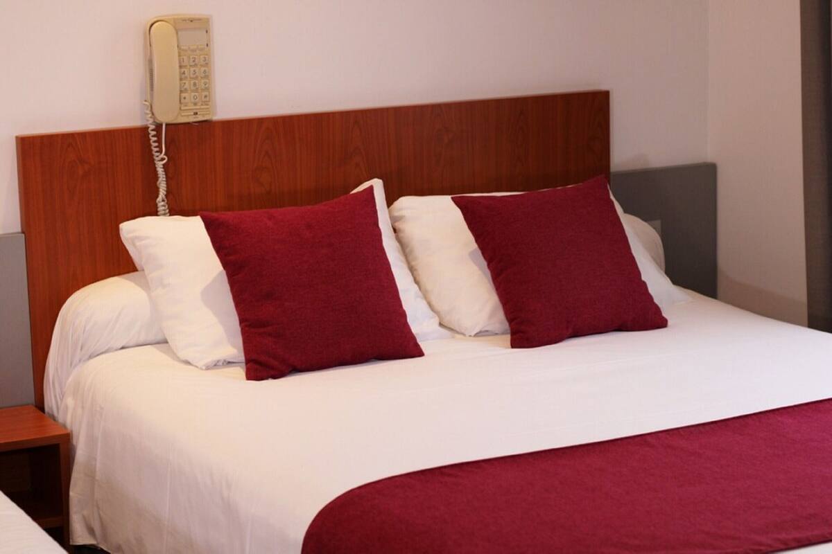A neatly made bed with white and red bedding, a wooden headboard, and a bedside telephone.