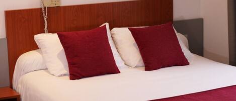 A neatly made bed with white and red bedding, a wooden headboard, and a bedside telephone.