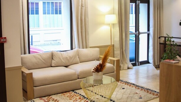 A modern living room with a beige sofa, a glass coffee table, and a patterned rug. - Hotel Little (Paris)
