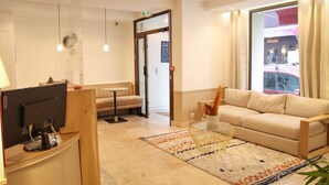 A hotel lobby with a sofa, a small table, a computer desk, and a large window with curtains. - Hotel Little (Paris)