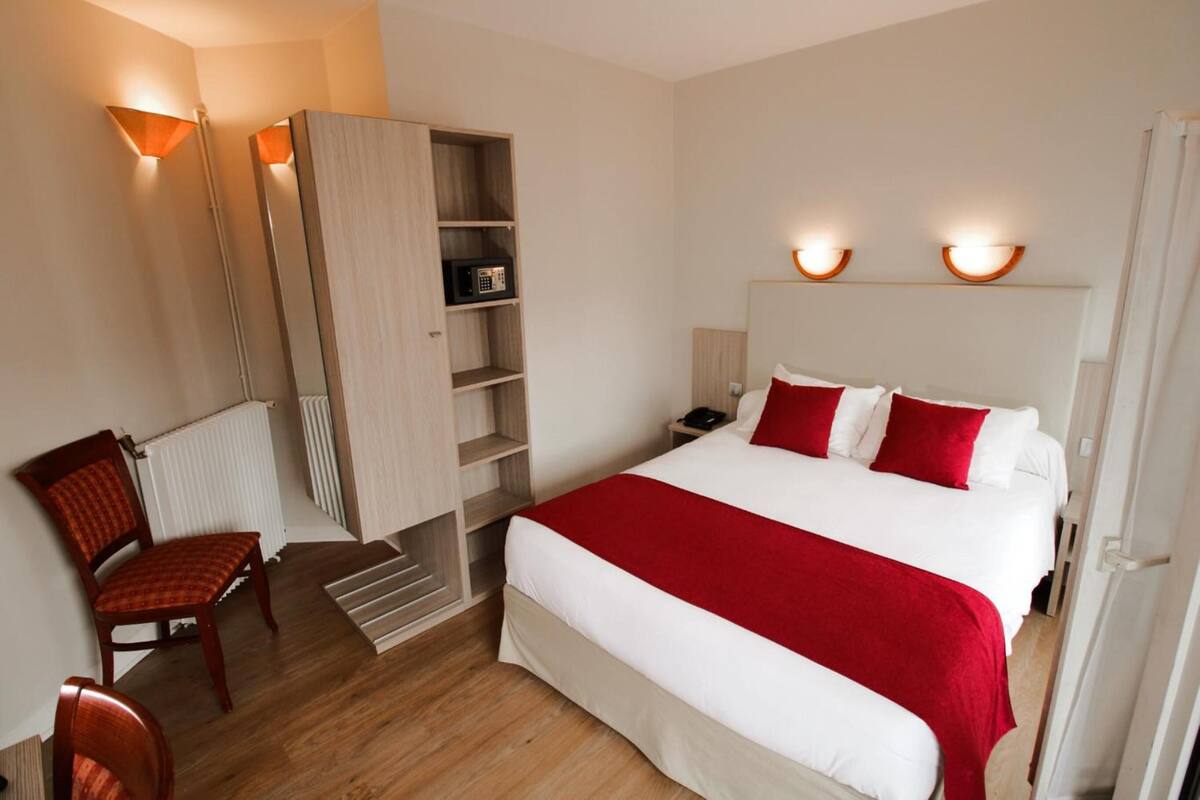 A hotel room with a bed, a chair, a wardrobe, and a nightstand.