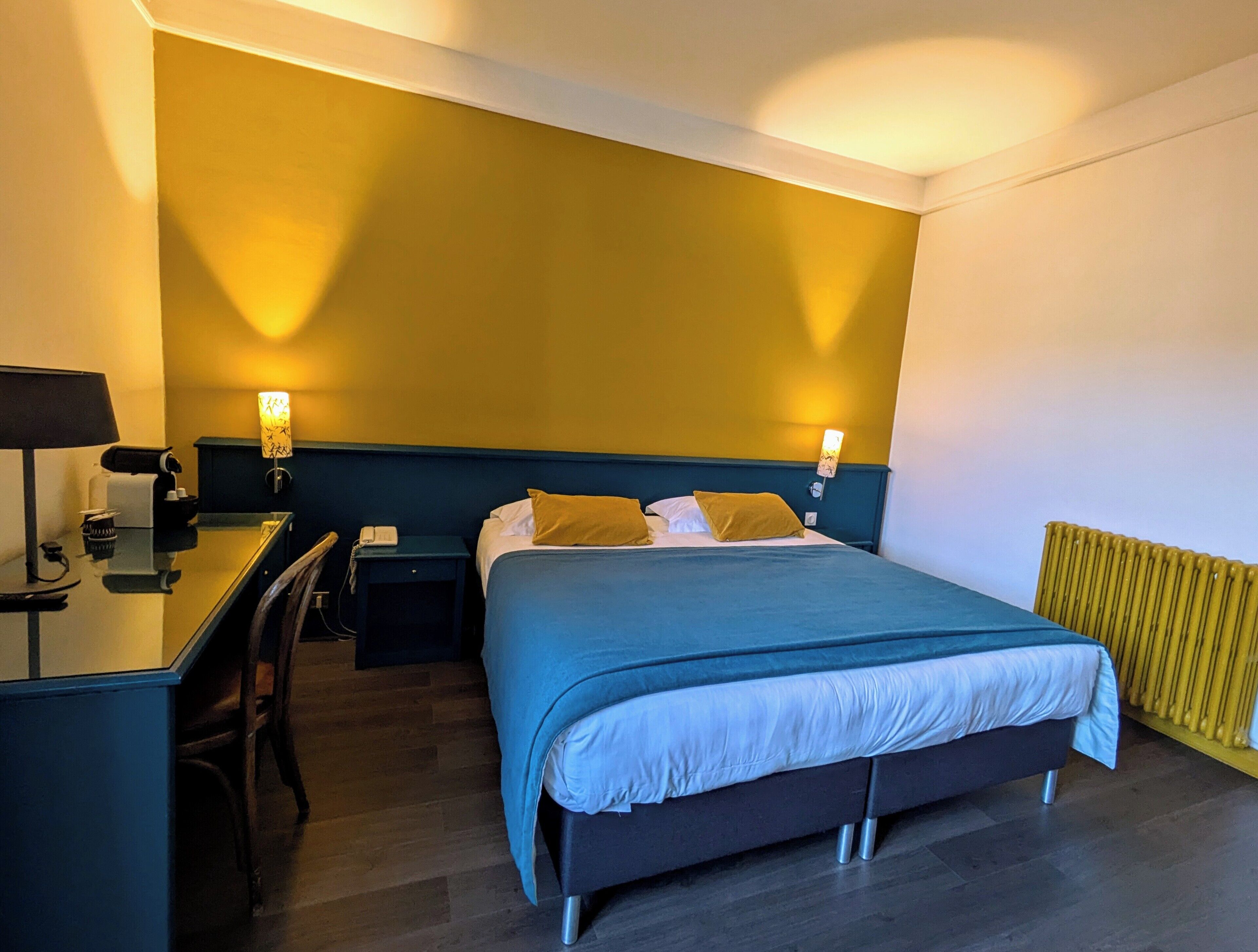 Ein Hotelzimmer mit Bett, Nachttisch, Lampe und Schreibtisch mit Stuhl.