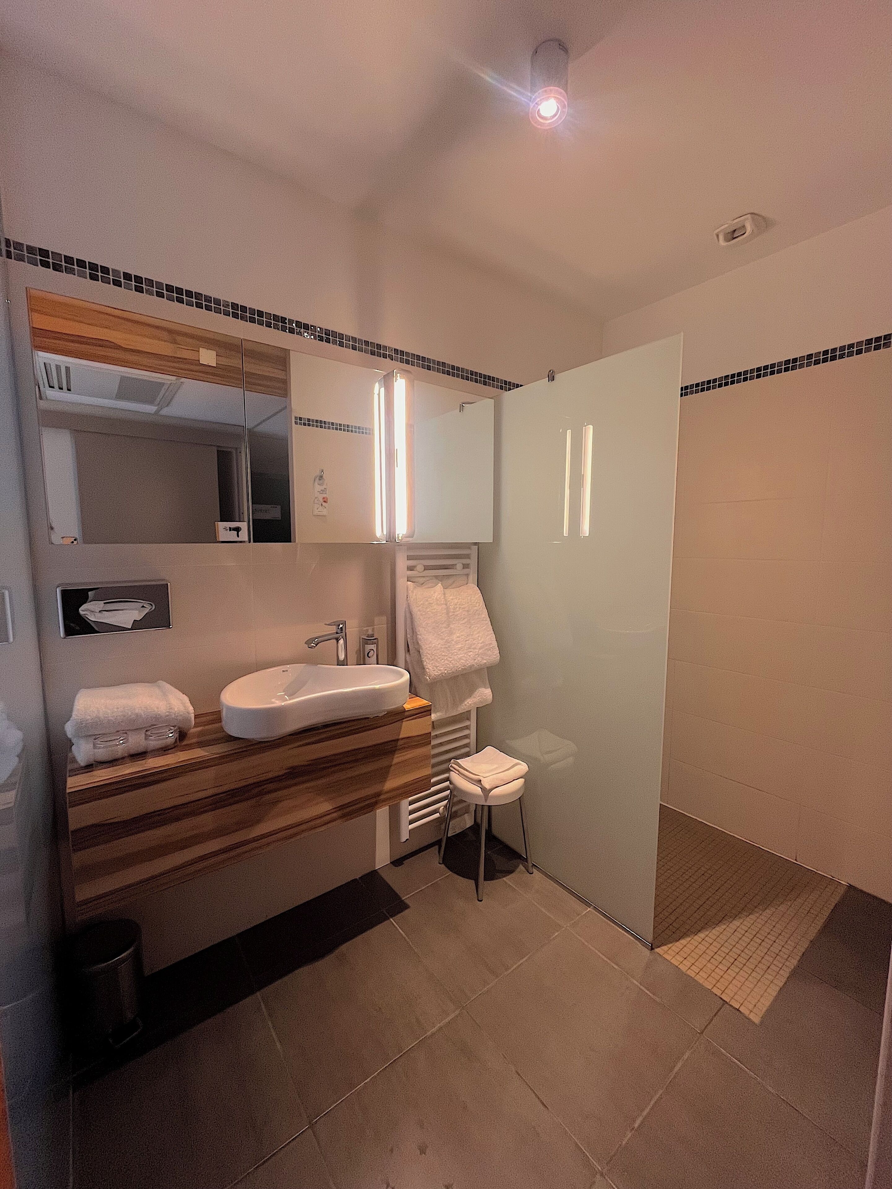 Un baño moderno con lavamanos, espejo, toallero y zona de ducha.