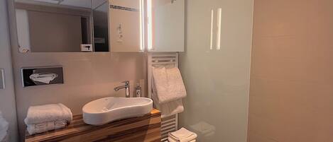Un baño moderno con lavamanos, espejo, toallero y zona de ducha.