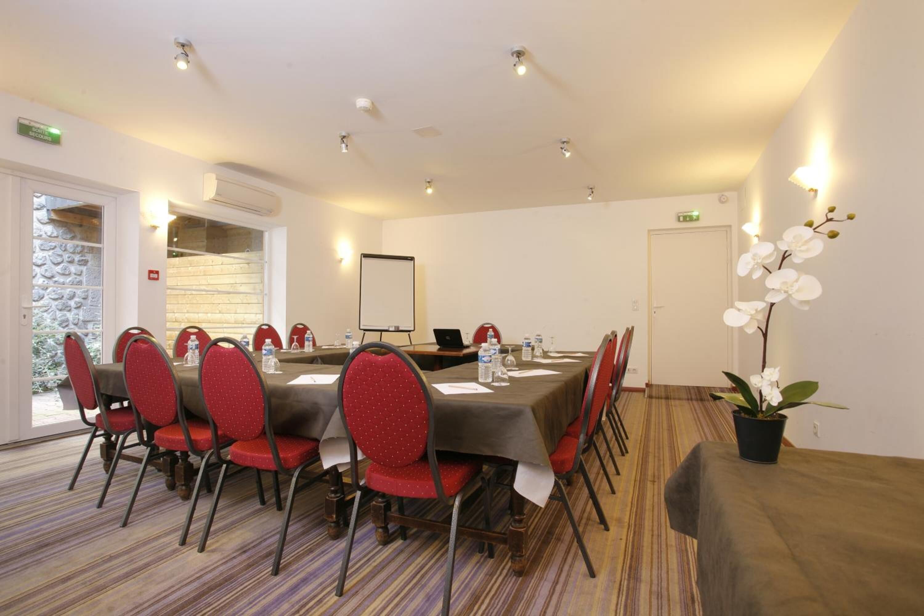 Une salle de conférence avec une longue table, des chaises rouges, un ordinateur portable et un tableau blanc.
