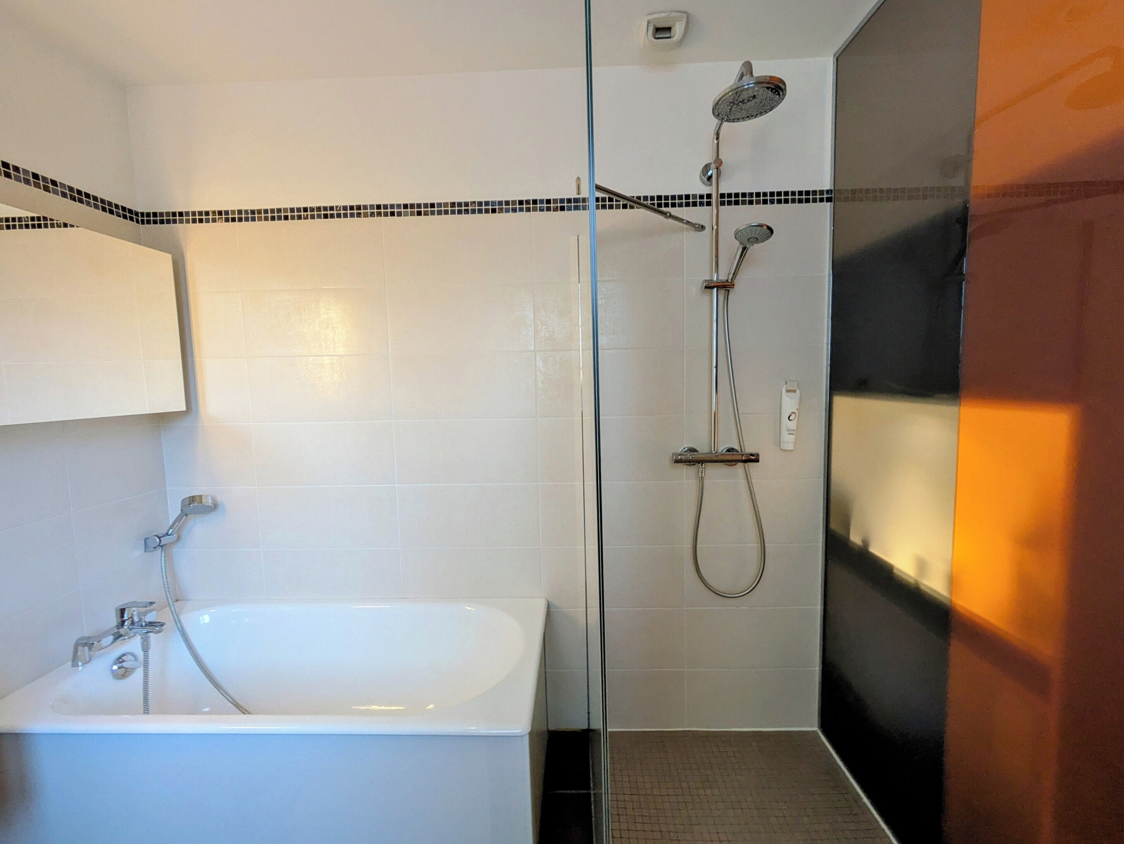 Un baño moderno con bañera, cabina de ducha con mampara de cristal y suelo de baldosas.
