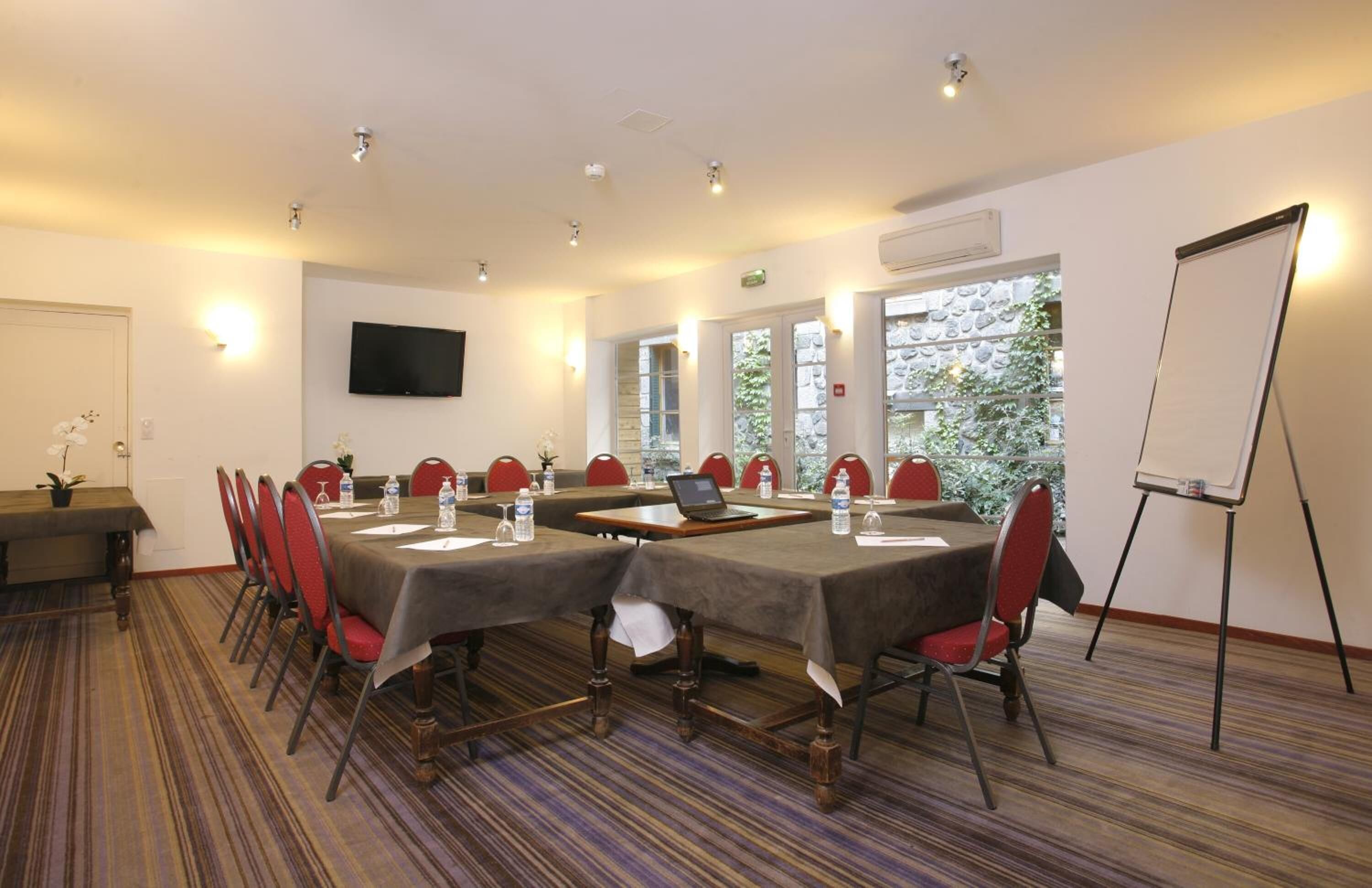 Una sala de conferències amb una taula llarga, cadires vermelles, un portàtil, ampolles d'aigua i una pissarra blanca.
