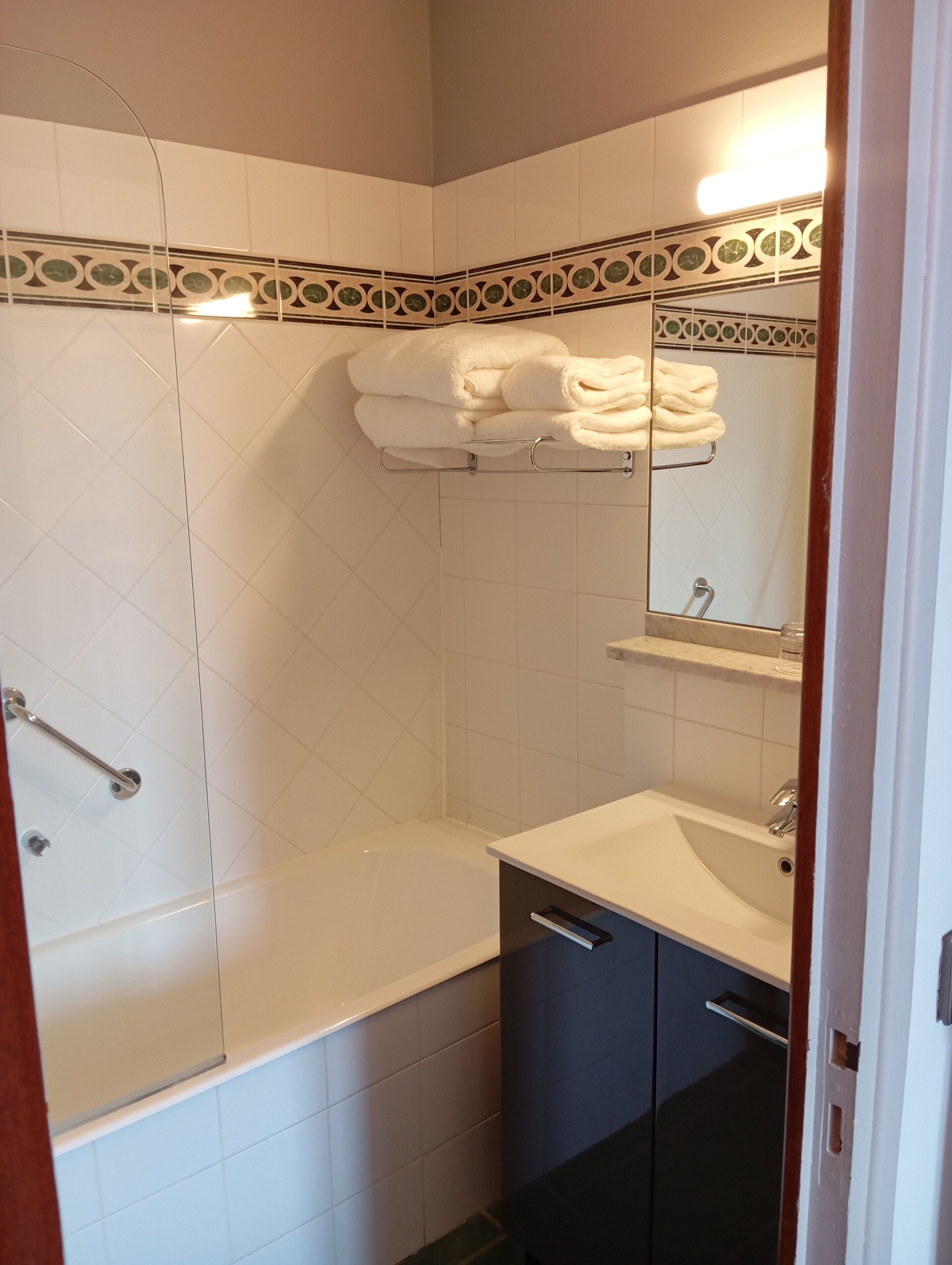 Un baño con bañera, lavabo y ducha. Hay un perchero con toallas y un espejo sobre el lavabo.