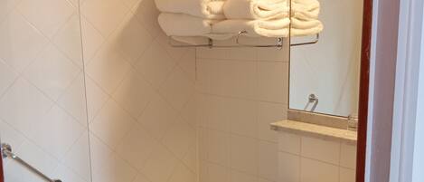 Un baño con bañera, lavabo y ducha. Hay un perchero con toallas y un espejo sobre el lavabo.