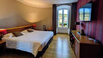 Hotelkamer met een groot bed, een bureau, een stoel, een televisie en een raam met uitzicht op gebouwen.