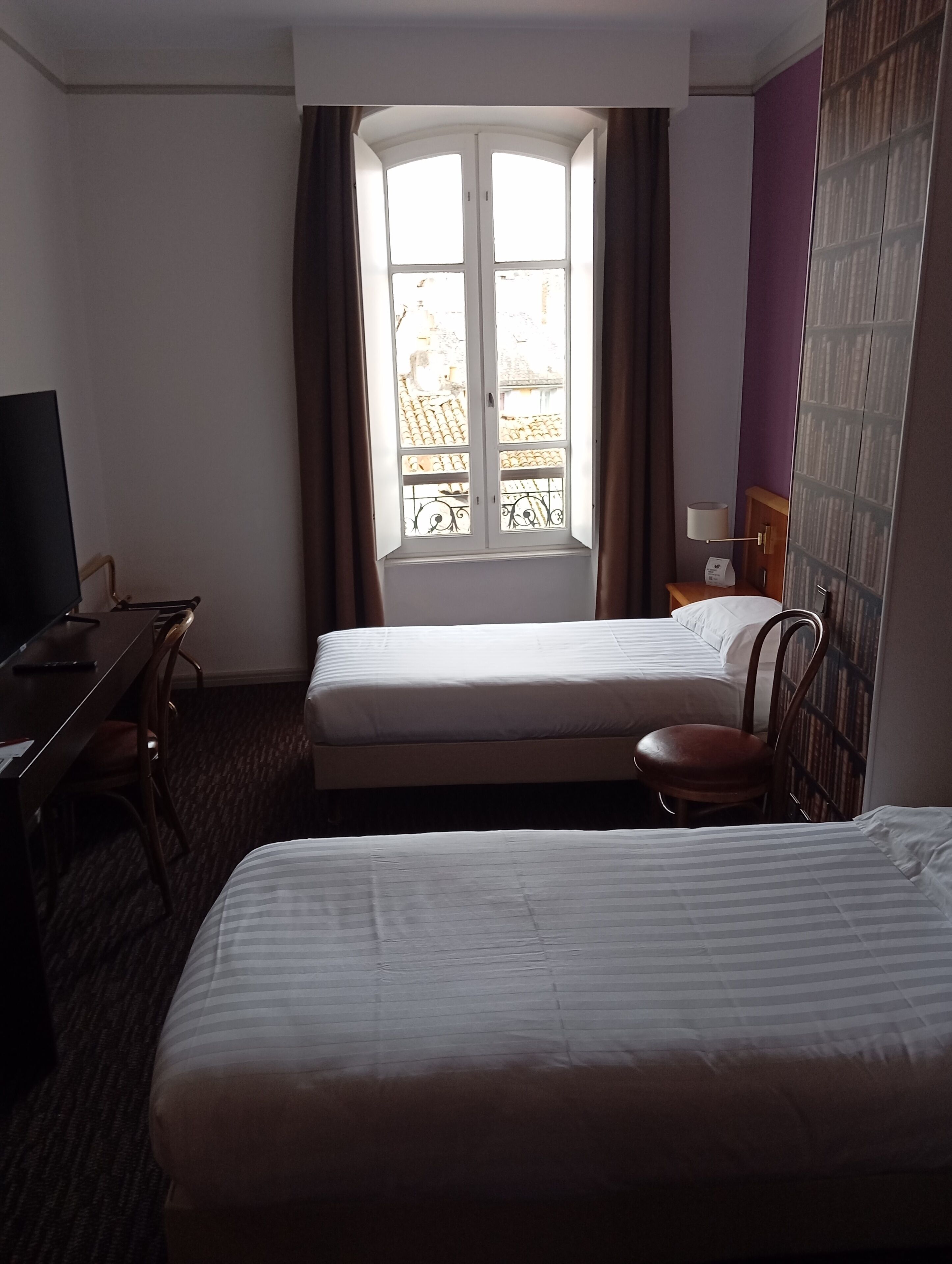 A hotel room with two beds, a desk, a chair, a TV, and a window with curtains.