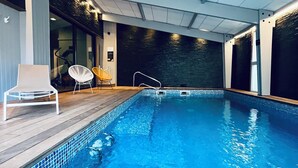Une piscine intérieure dotée d’une terrasse en bois, de deux chaises longues et d’un mur au motif texturé.