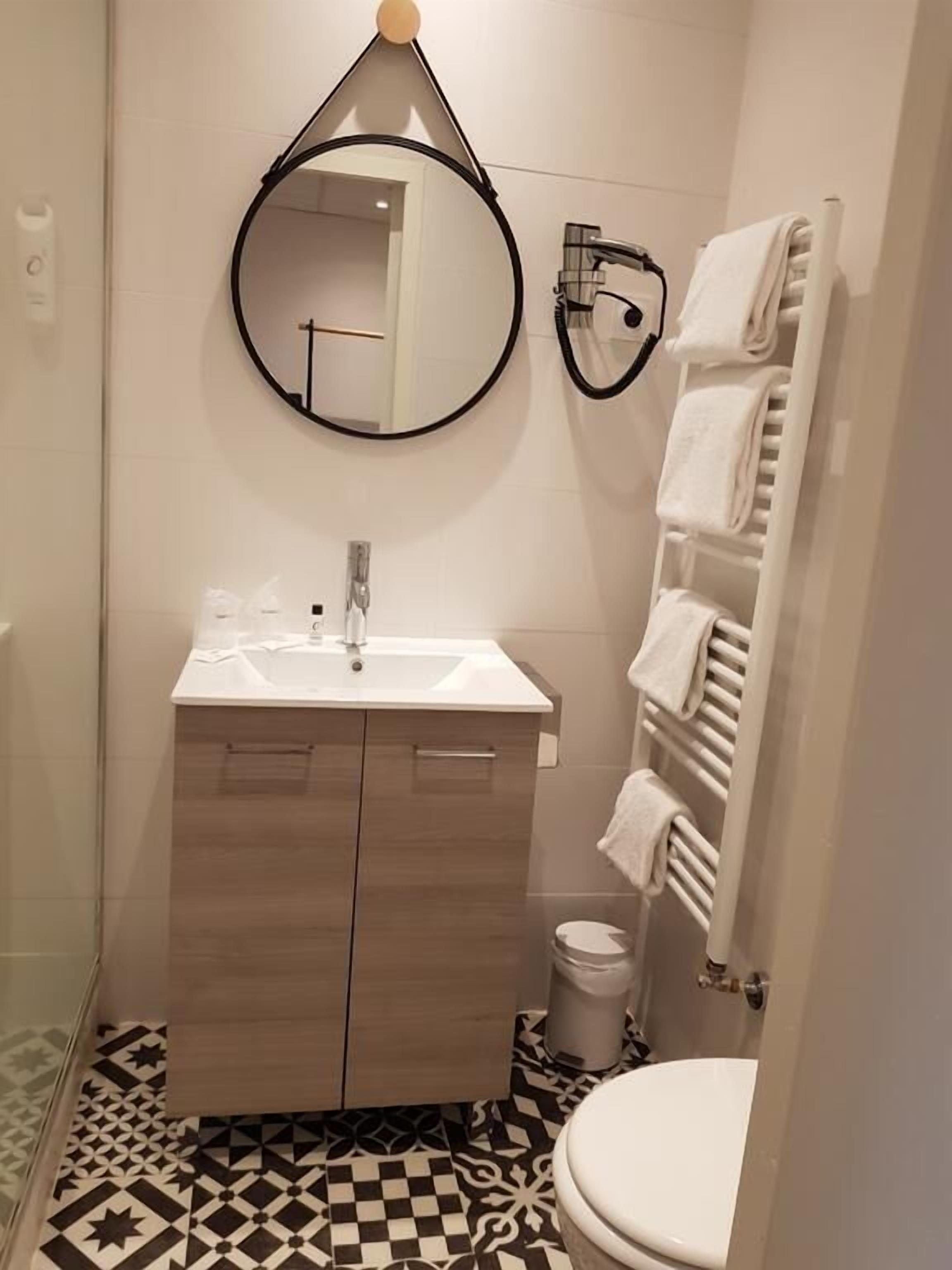 Un baño con tocador de madera, un espejo redondo, un inodoro y un perchero para toallas.
