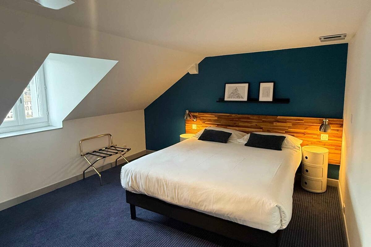 Ein modernes Hotelzimmer mit einem großen Bett, einem hölzernen Kopfteil, einem kleinen Nachttisch und einem Fenster mit Aussicht.