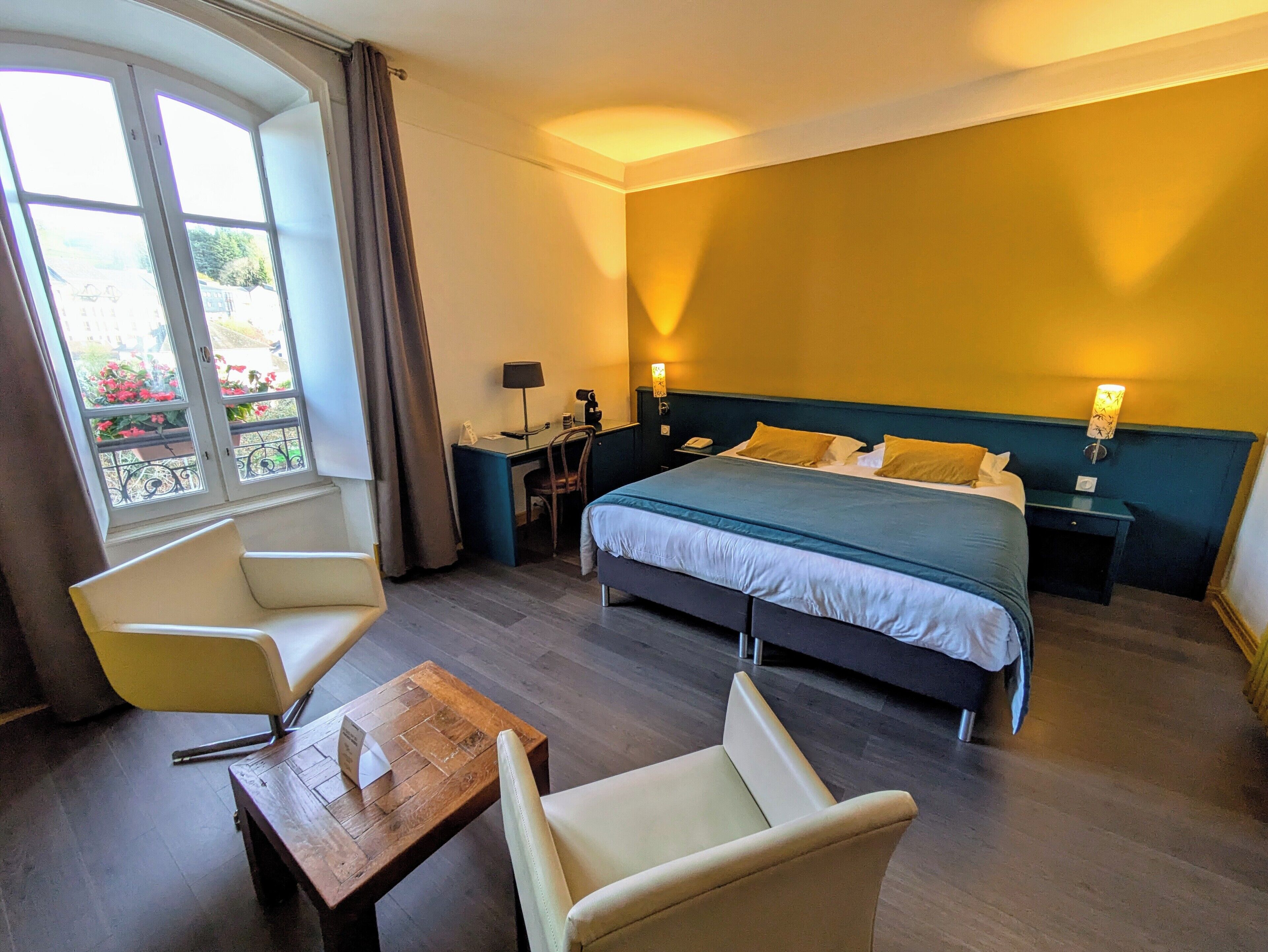 Habitación de hotel con cama, dos sillas, una mesita, un escritorio y una mesita de noche.