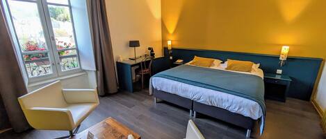 Habitación de hotel con cama, dos sillas, una mesita, un escritorio y una mesita de noche.