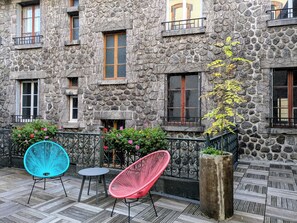 A stone building with multiple windows, a balcony with a metal railing, and outdoor seating with two chairs. - The Originals Boutique, Grand Hôtel St Pierre (Aurillac)