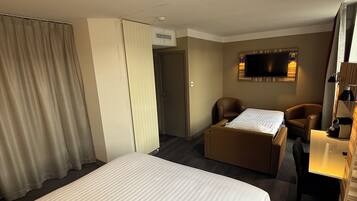 A hotel room with a large bed, a desk with a chair, a sofa, a television, and a window with curtains.