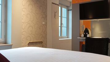 A hotel room with a large bed, a chair, a desk with a flat-screen TV, and a window.