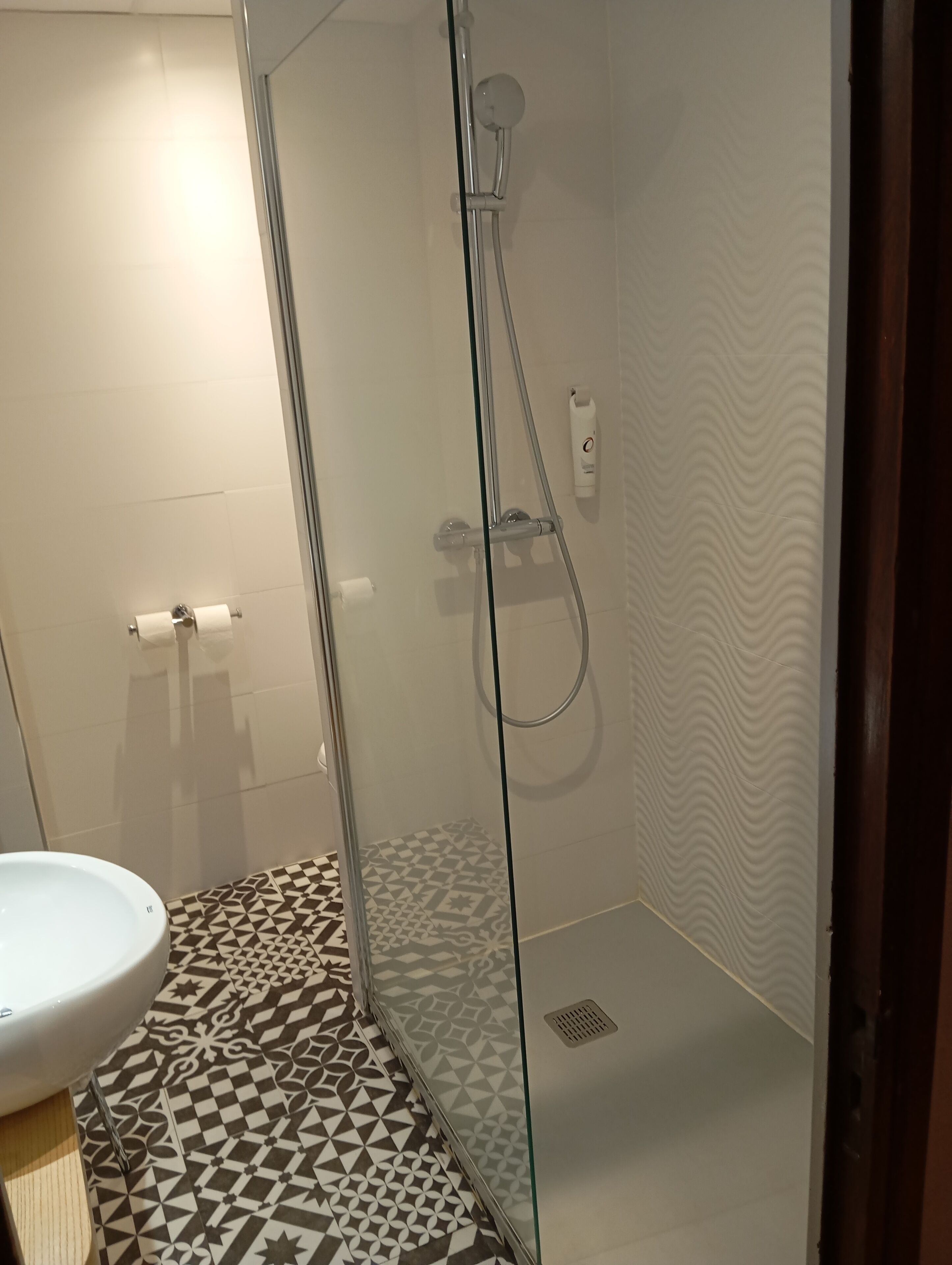 A modern bathroom with a glass-enclosed shower, a white sink, and patterned floor tiles.