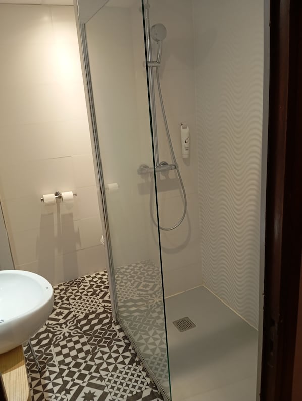 A modern bathroom with a glass-enclosed shower, a white sink, and patterned floor tiles.