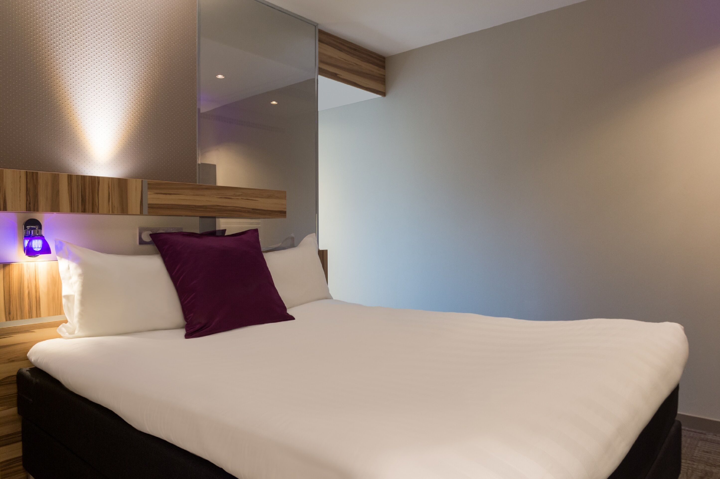 A modern hotel room with a large bed, a wooden headboard, and a mirror above the bed.