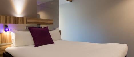 A modern hotel room with a large bed, a wooden headboard, and a mirror above the bed.