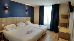 A hotel room with two beds, a desk, a TV, and a window with curtains. - Hotel Modern'Est (Paris)