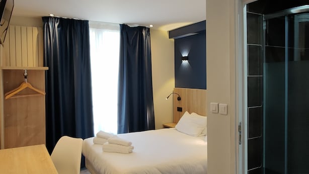 A hotel room with a bed, a desk, a chair, a wardrobe, a shower, and a window with curtains. - Hotel Modern'Est (Paris)