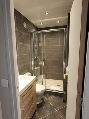 Un baño moderno con ducha envuelta en vidrio, un lavamanos blanco y un mueble de tocador de madera.