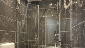 A modern bathroom with a black marble wall, a round sink, a mirror, a handheld showerhead, and a toilet. - Hotel Modern'Est (Paris)