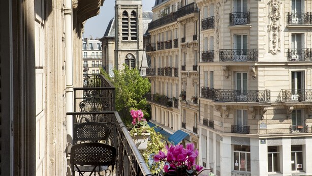 Une vue d’une rue parisienne, avec ses bâtiments historiques, une tour et des balcons dotés de garde-corps.