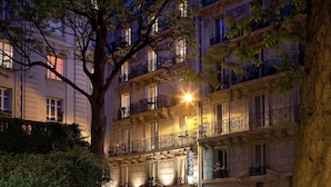 Un hôtel à plusieurs étages doté de balcons, une enseigne indiquant qu’il s’agit d’un hôtel, et un arbre au premier plan.
