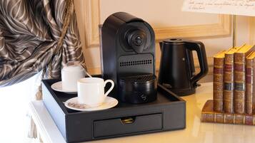 A coffee machine, a cup, a saucer, a tray, a kettle, and a stack of books on a table.