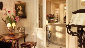 Une pièce élégante et bien éclairée, dotée d’un décor classique, comprenant un portrait encadré, un vase de fleurs, une table avec une lampe et un piano.
