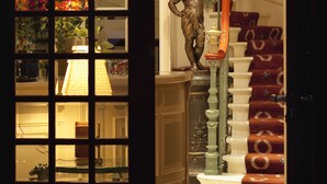 Un magnifique escalier, recouvert d’un tapis rouge, orné d’une statue et éclairé par une lampe.