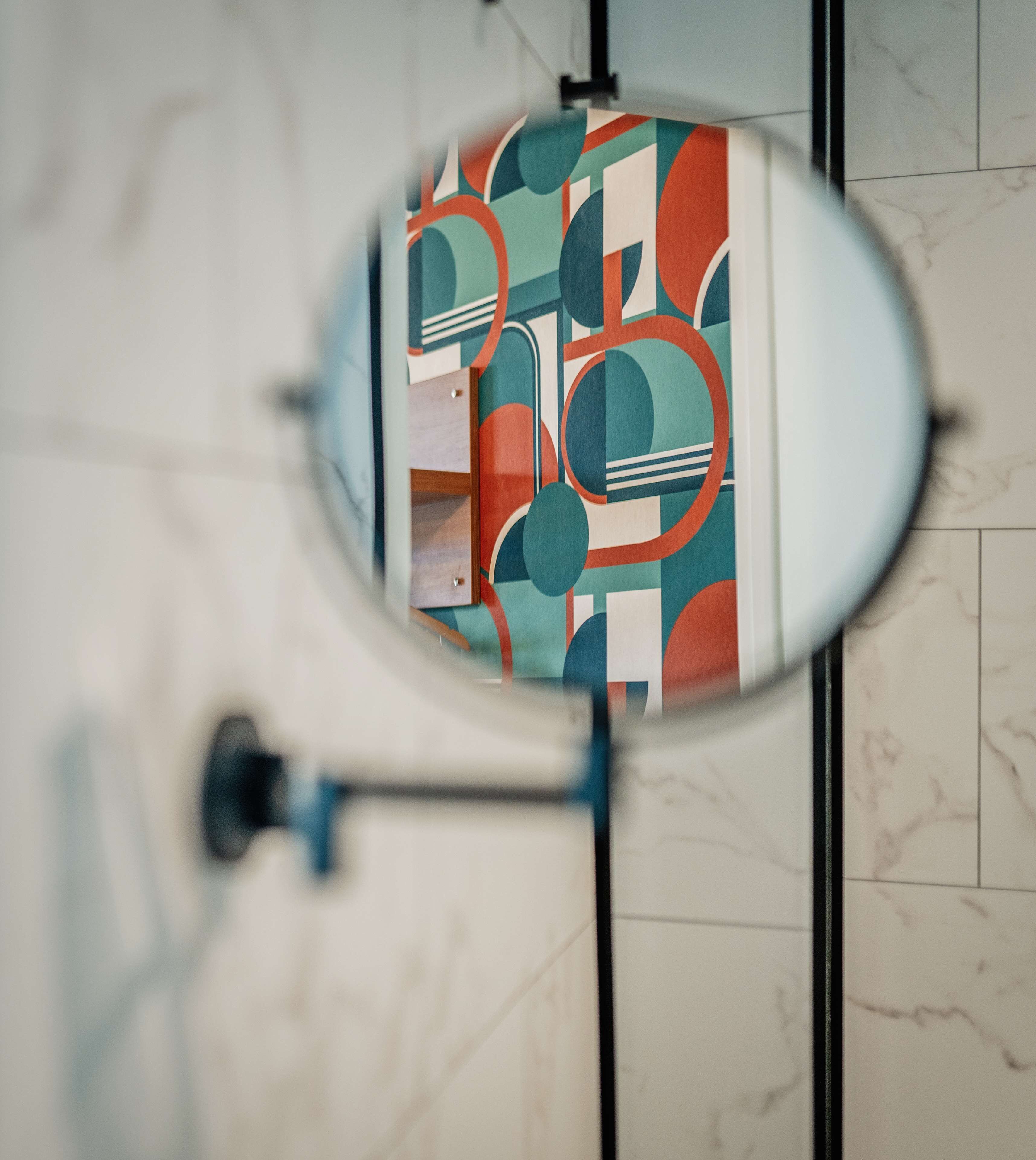 A toilet with a mirror reflecting a bathroom with a tiled floor and a wall-mounted toilet paper holder.
