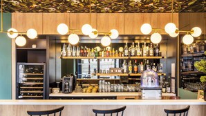 Zona bar con scaffali in legno pieni di diverse bottiglie, una macchina da caffè e un juke-box. Davanti al bancone ci sono tre sedie nere.