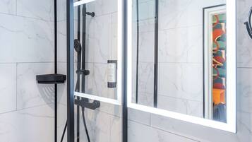 Un baño moderno con ducha de vidrio, un espejo grande y un lavamanos blanco.