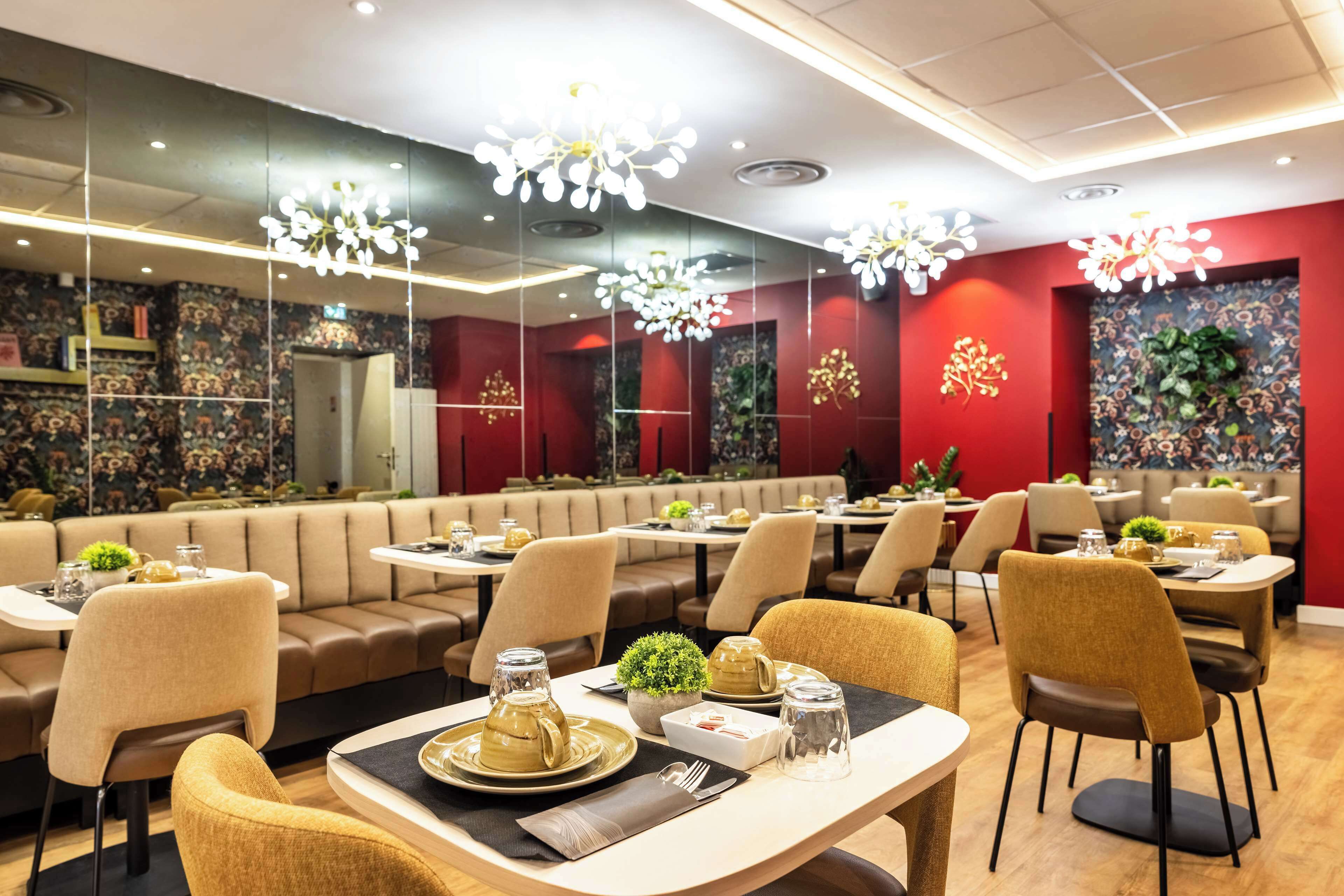 Un restaurant moderne avec des banquettes et des tables, un éclairage décoratif et un mur rouge vif orné de motifs floraux.
