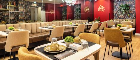 A modern restaurant with booths and tables, decorative lighting, and a vibrant red wall with floral patterns.