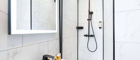 A modern bathroom with a white marble tile wall, a black showerhead, and a white sink with a mirror above it.