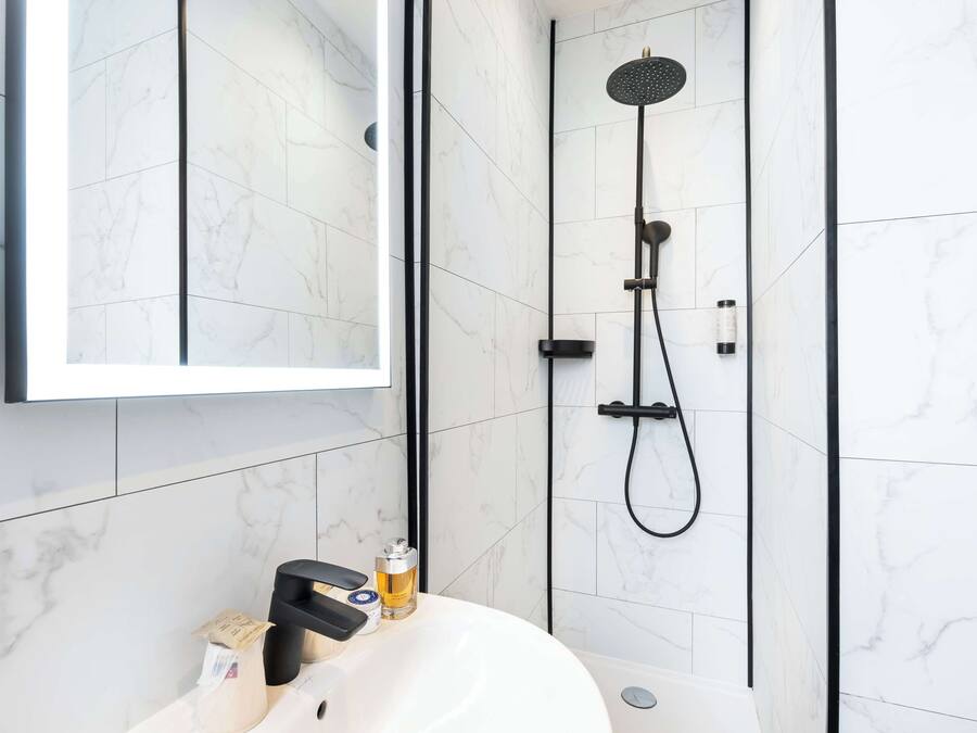 A modern bathroom with a white marble tile wall, a black showerhead, and a white sink with a mirror above it.