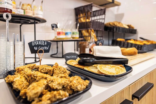 Un bufé con diversos alimentos, entre ellos pollo frito, panqueques y granola.