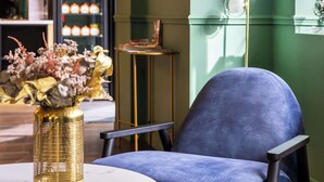 Un interno moderno con una poltrona blu, un tavolino con un vaso dorato e una lampada a parete.